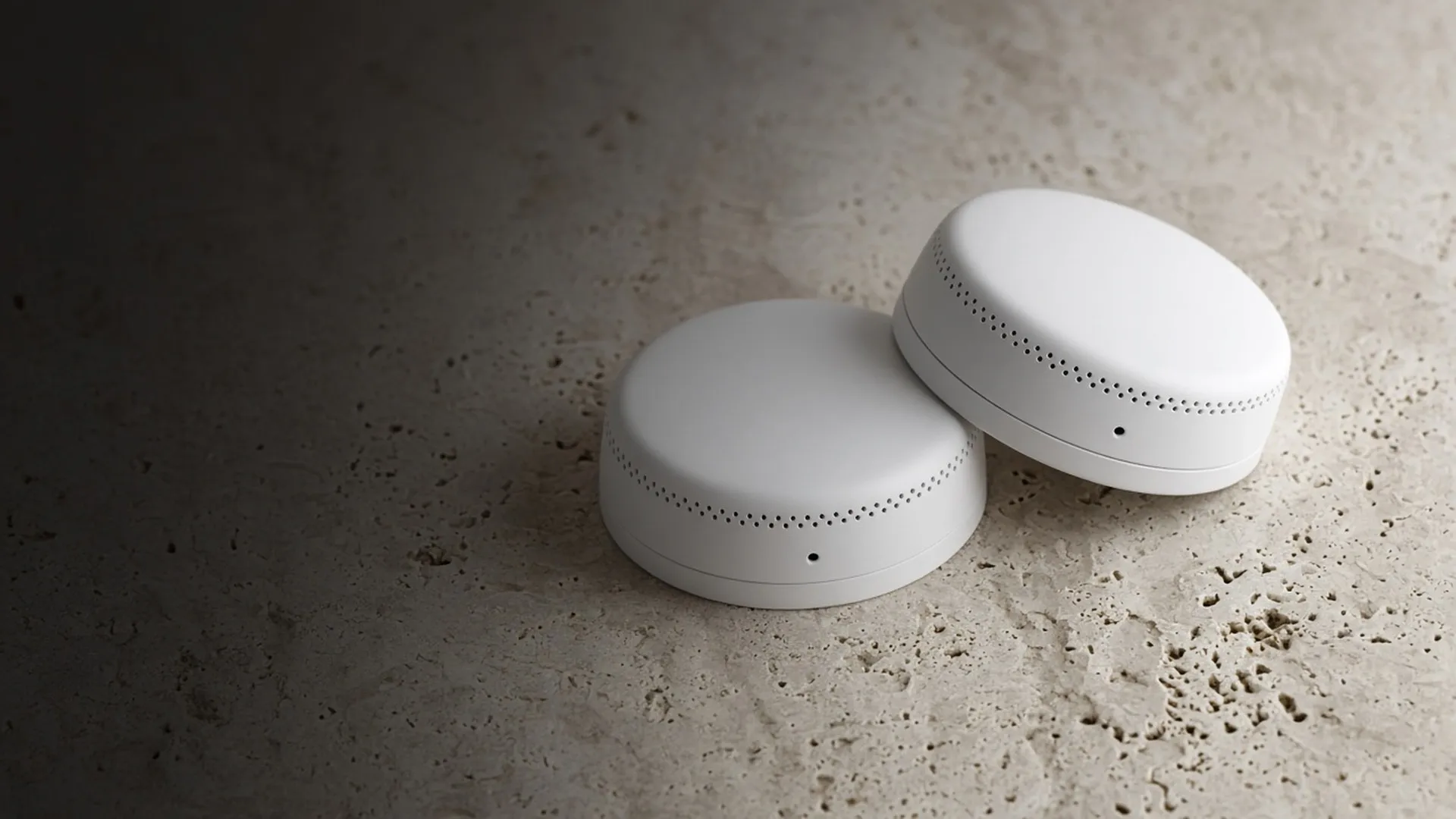 Two plain unbranded smoke alarms resting on a pale stone surface