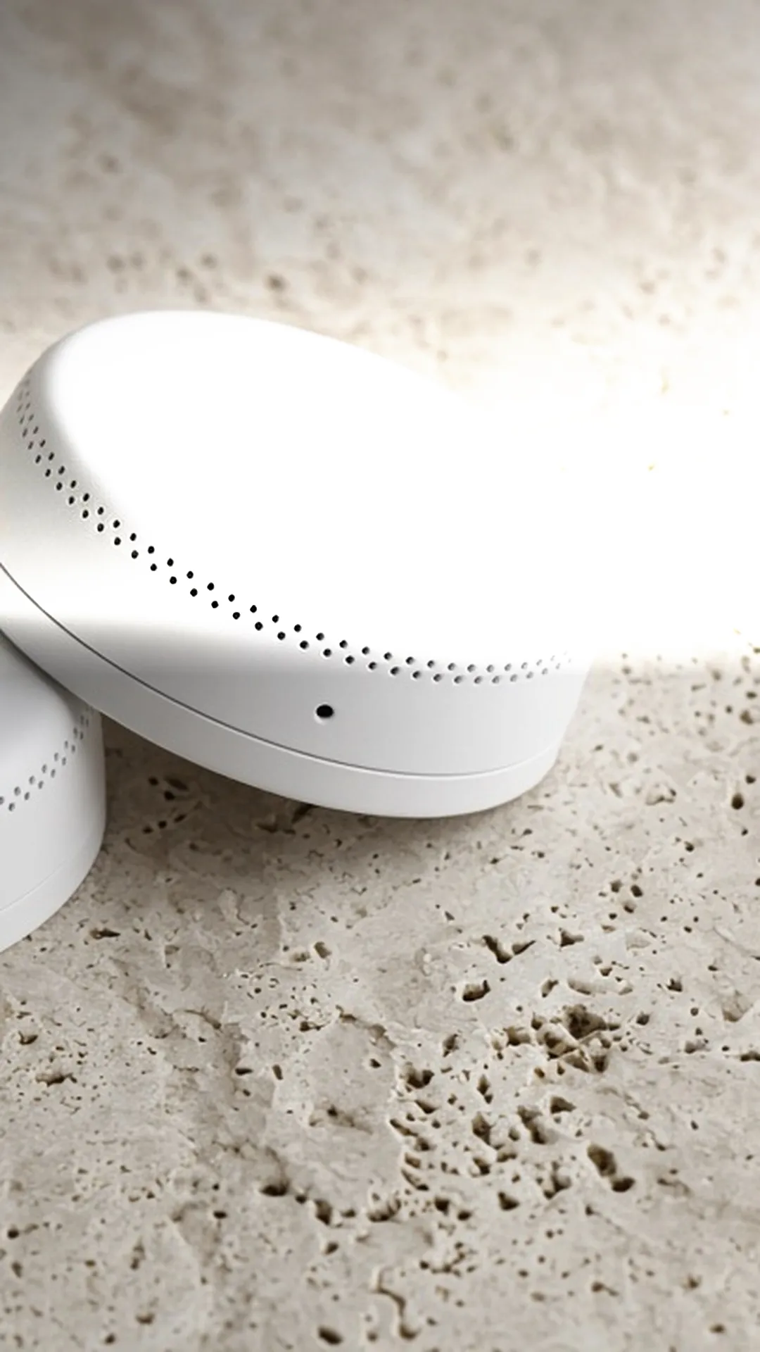 Two plain unbranded smoke alarms resting on a pale stone surface