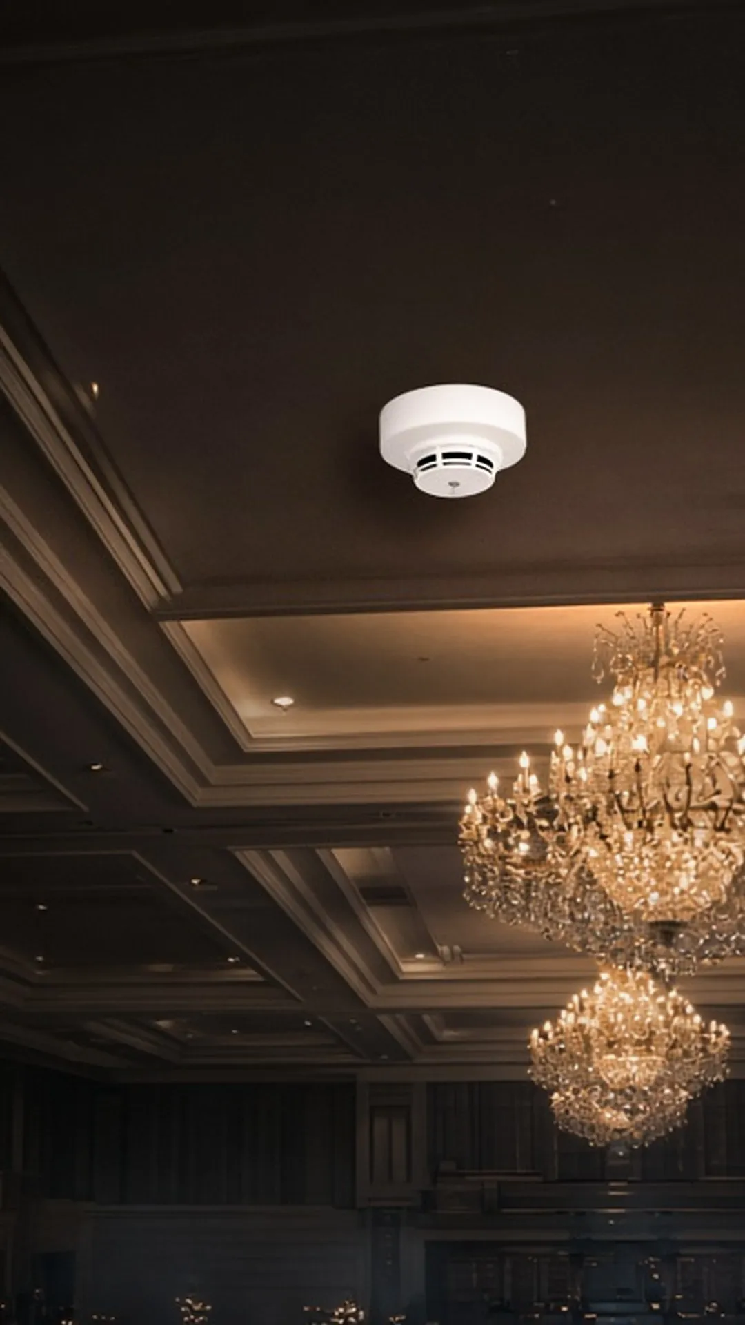 A ceiling-mounted smoke detector in an elegant event hall